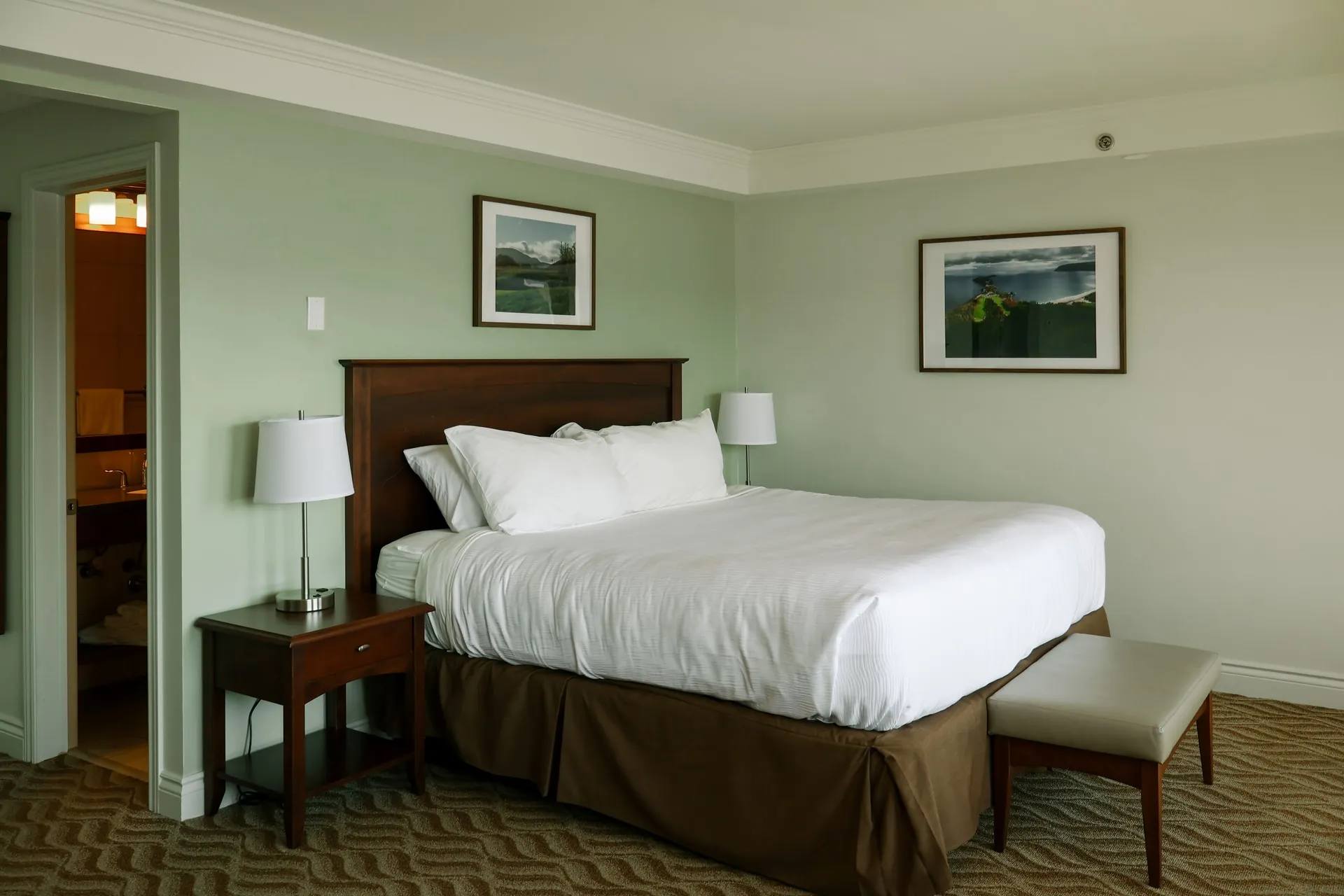 A guest room with a white bed, dark wood headboard, and framed highland landscapes.