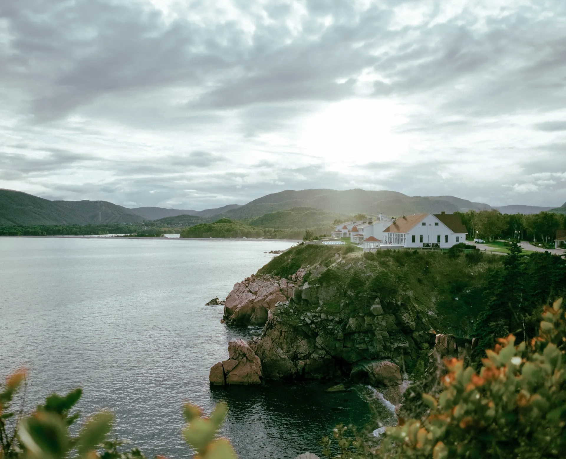 The Keltic Resort main building on a rocky headland above the Atlantic, with forested hills across the water.