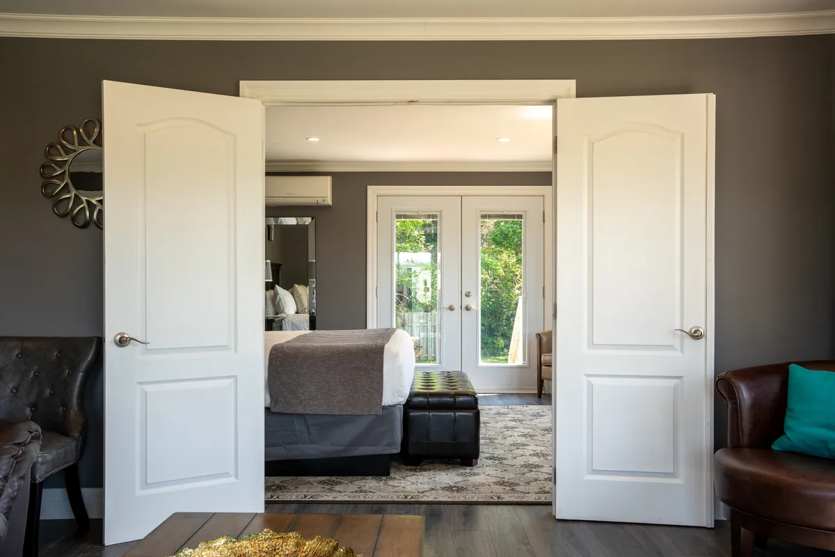 Open white double doors framing a bedroom with a bed and glass doors leading to an outdoor deck.
