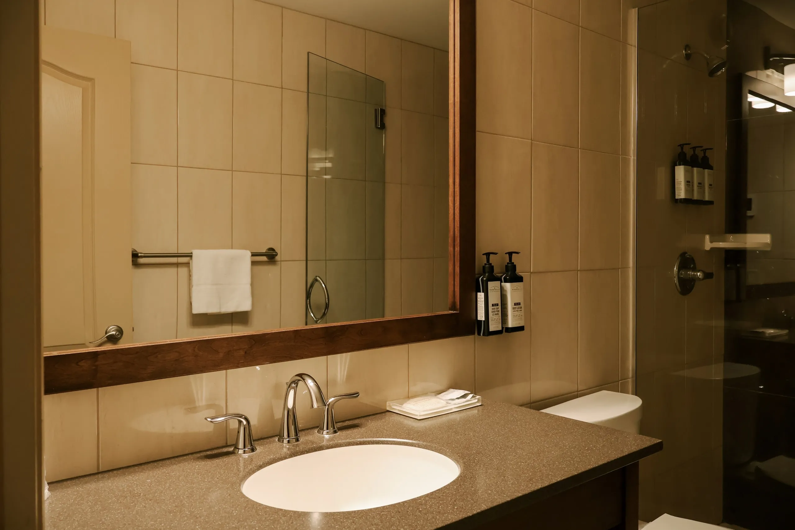 A guest bathroom with a stone vanity, an oval sink, a wood-framed mirror, and a glass shower.