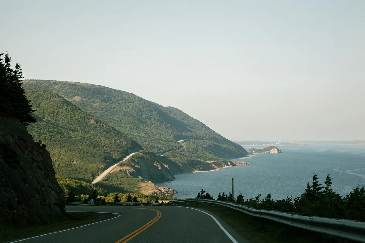 The Cabot Trail winding along a forested coastal mountain with the Atlantic Ocean beyond.