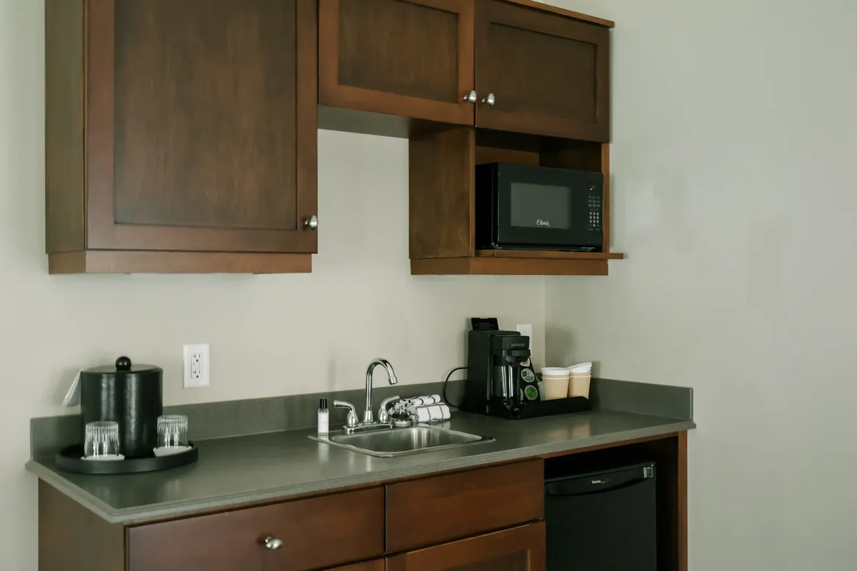 A kitchenette with wood cabinets, a sink, coffee maker, microwave, and mini fridge.