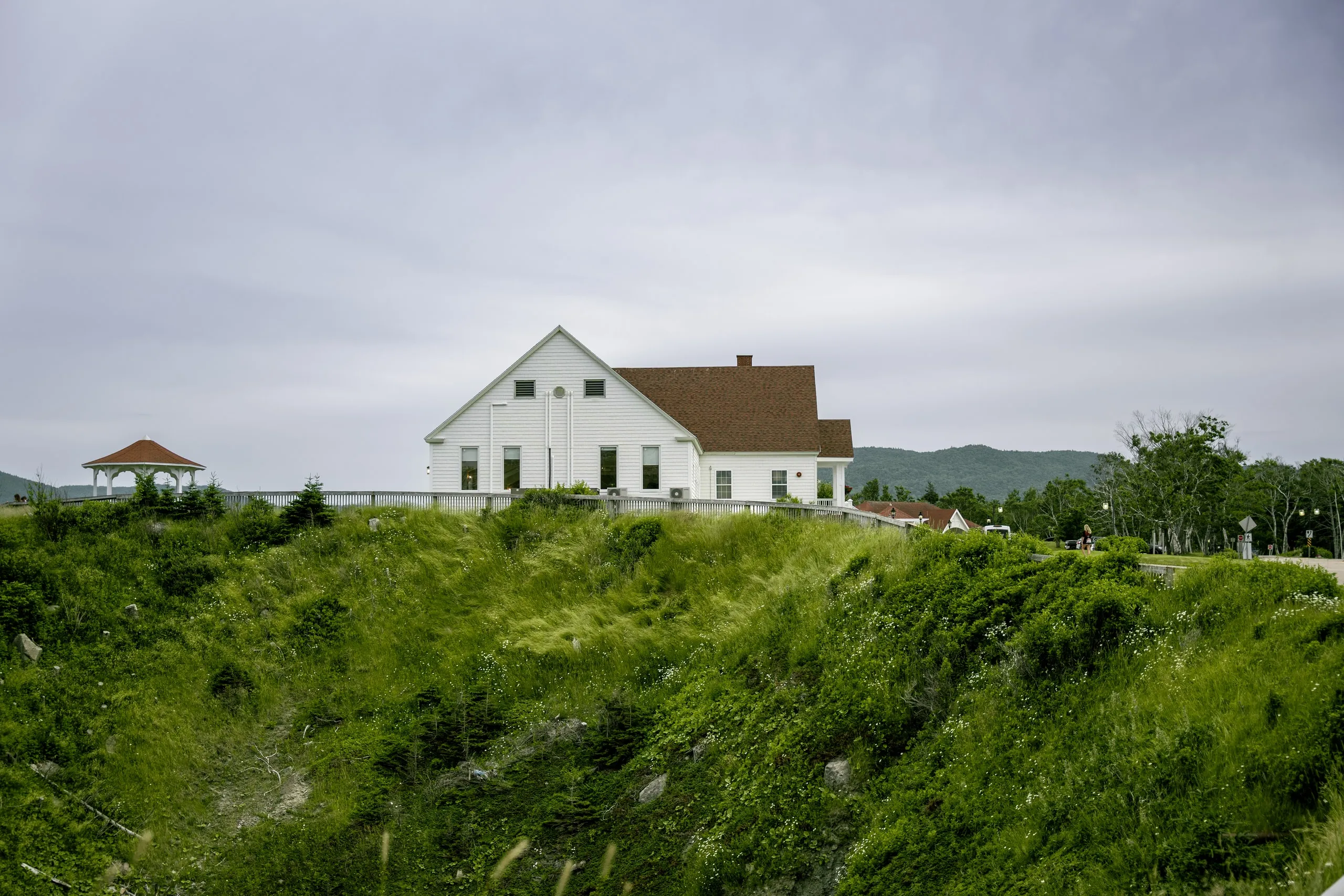 The white Keltic Lodge on a grassy bluff, with a gazebo and forested hills behind