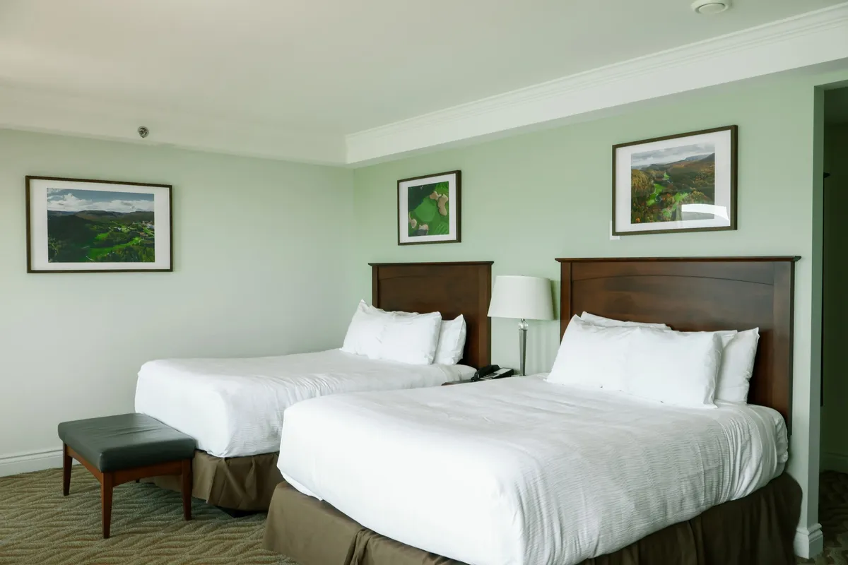 A guest room with two double beds, sage-green walls, and framed landscape photographs above the headboards.
