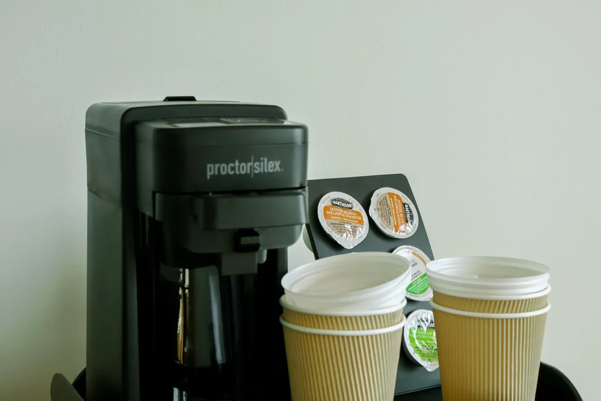 A coffee maker with stacked paper cups and single-serve coffee pods.