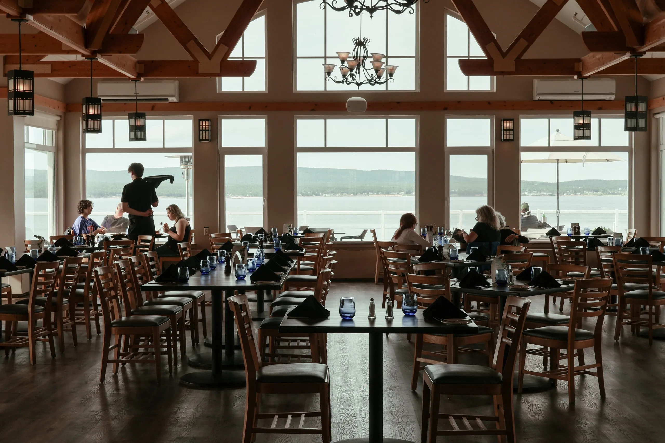 Guests dining in the Arduaine restaurant under timber beams, with floor-to-ceiling windows looking out to the Atlantic.