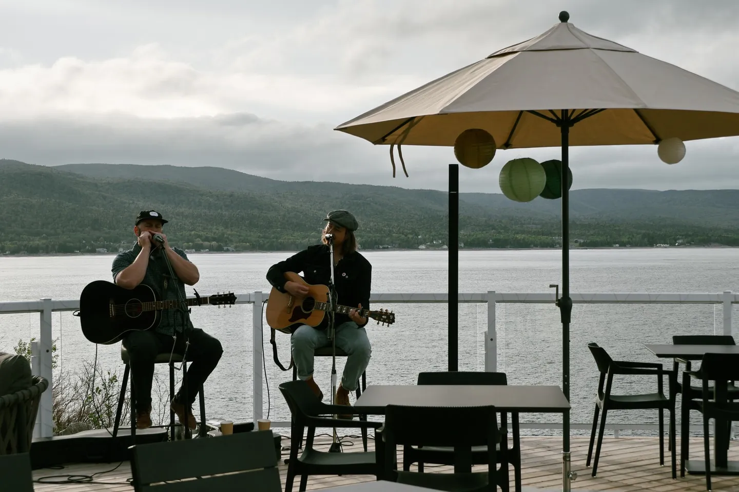 Two musicians performing on an oceanfront patio under an umbrella.