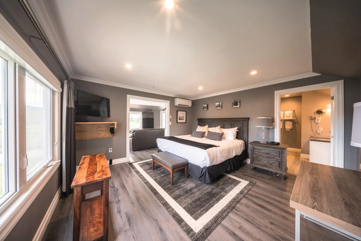 A bedroom with a king bed, grey walls, a wooden bench, and a doorway to the bathroom.