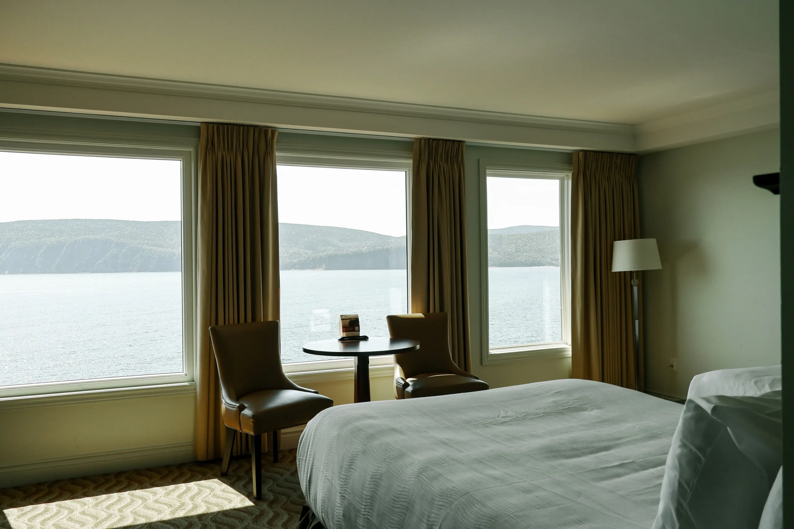 A guest room with a king bed and a table for two set in front of windows looking onto the water.