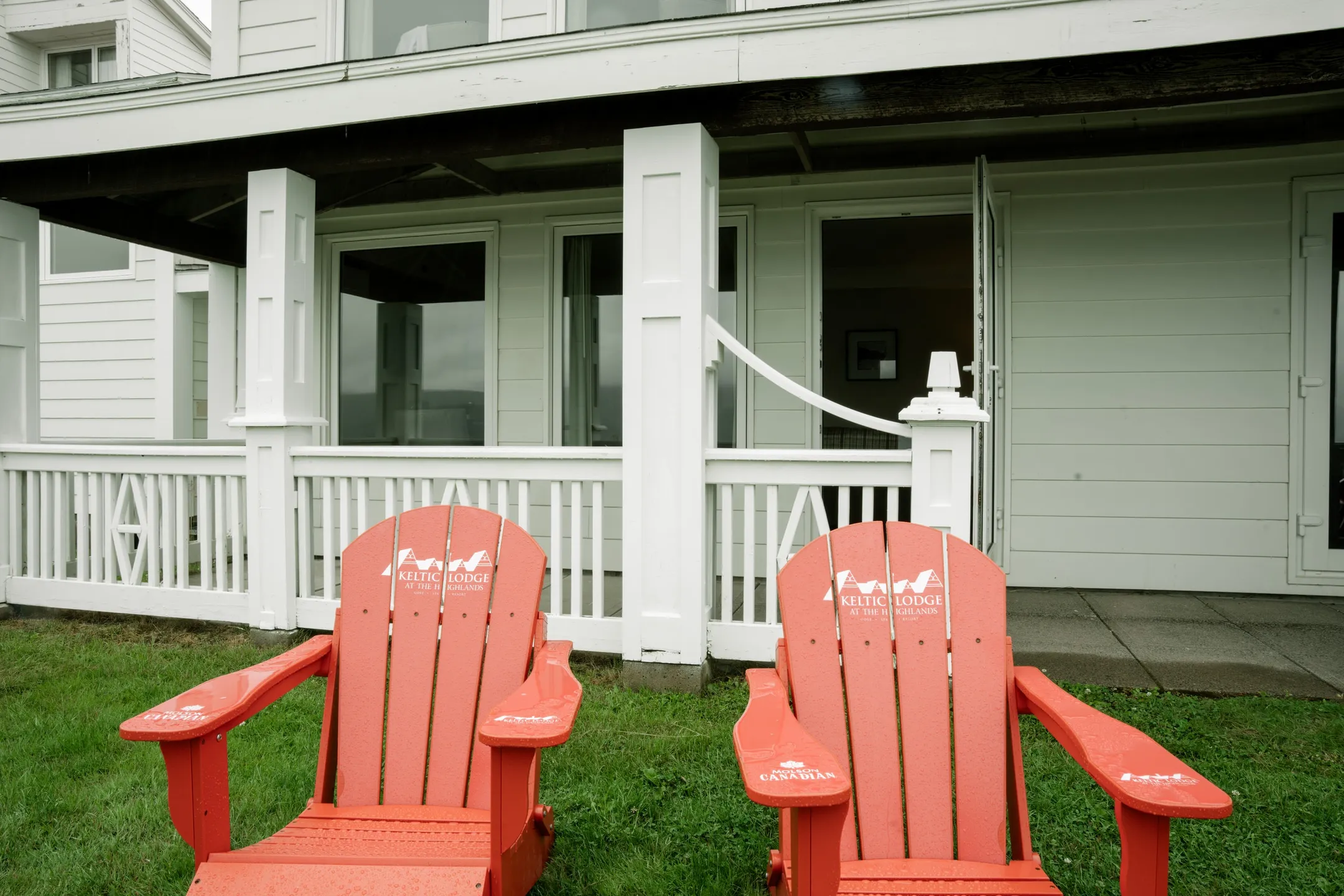 Two red chairs on the grass in front of a white porch and patio doors.