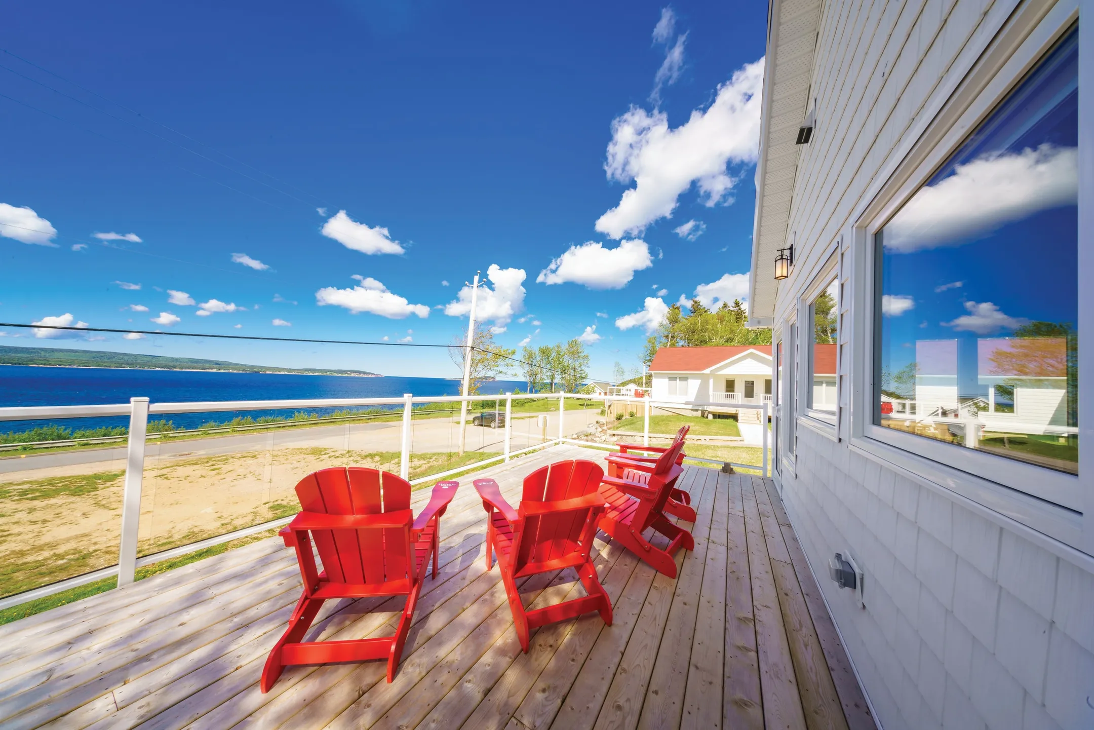 A wooden deck with two red Adirondack chairs overlooking the water and distant hills.