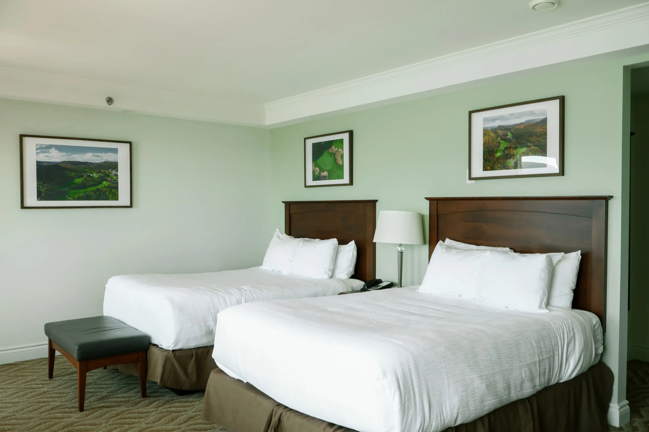 A twin room with sage-green walls, dark wood headboards, and framed landscape photographs.