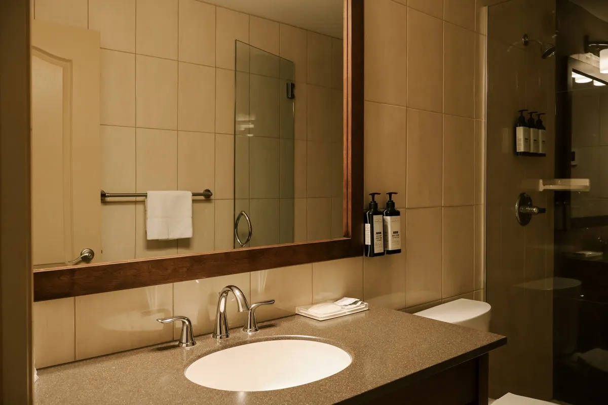A studio suite bathroom with a stone vanity, a wood-framed mirror, and a glass shower.