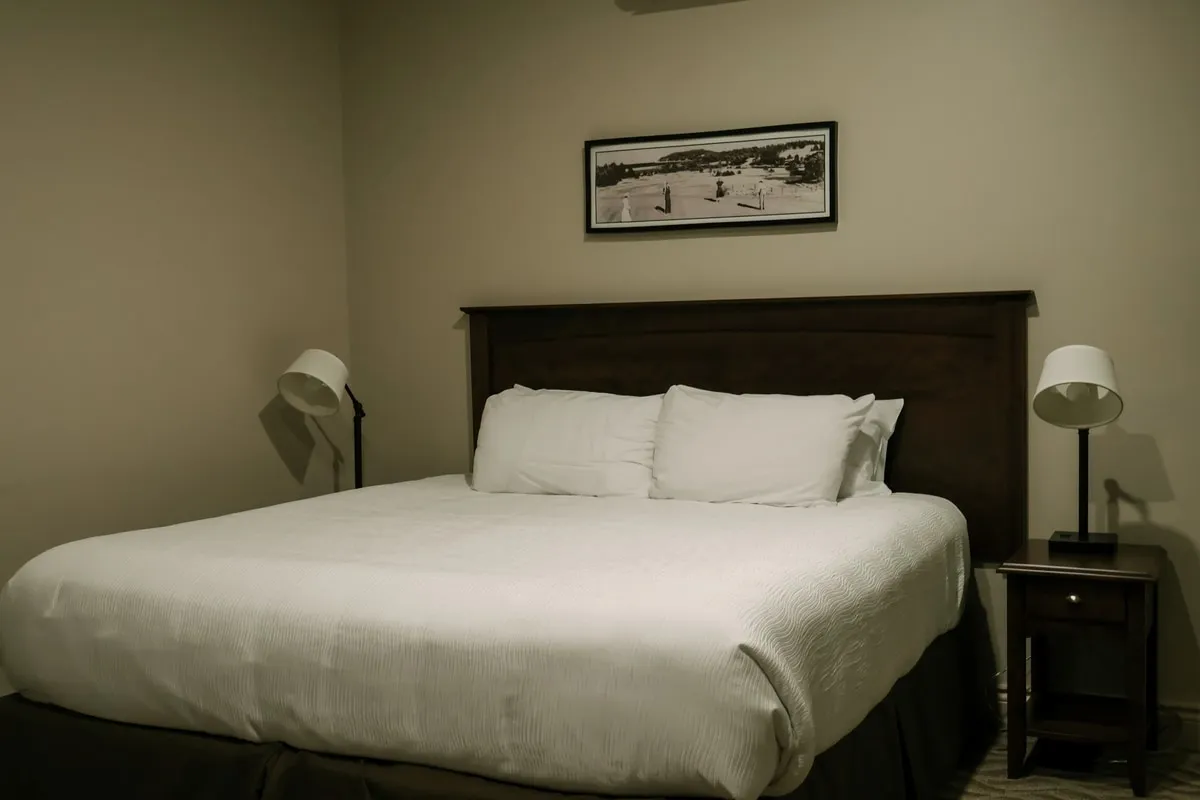 A studio suite bedroom with a king bed, a dark wood headboard, and a framed coastal photograph above it.