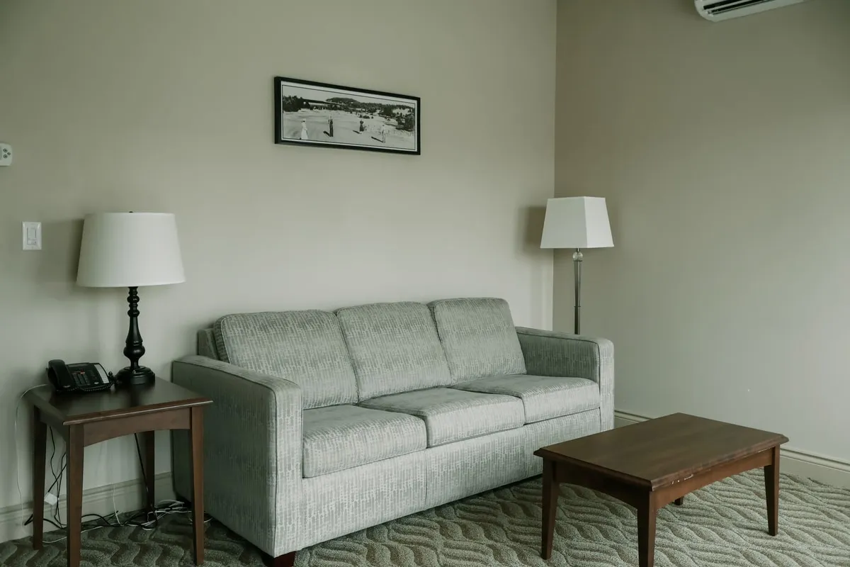 A studio suite living area with a grey sofa, a wood coffee table, and lamps beside the sofa.