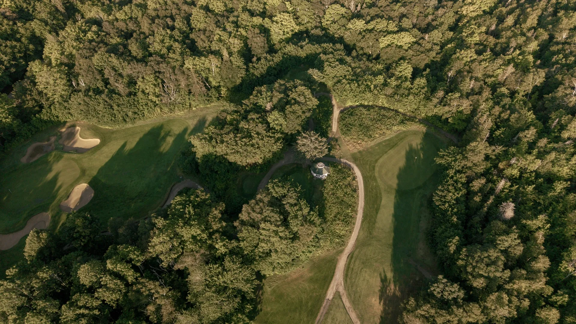 Aerial view of a tree-lined fairway with sand bunkers and a small building among the woods.