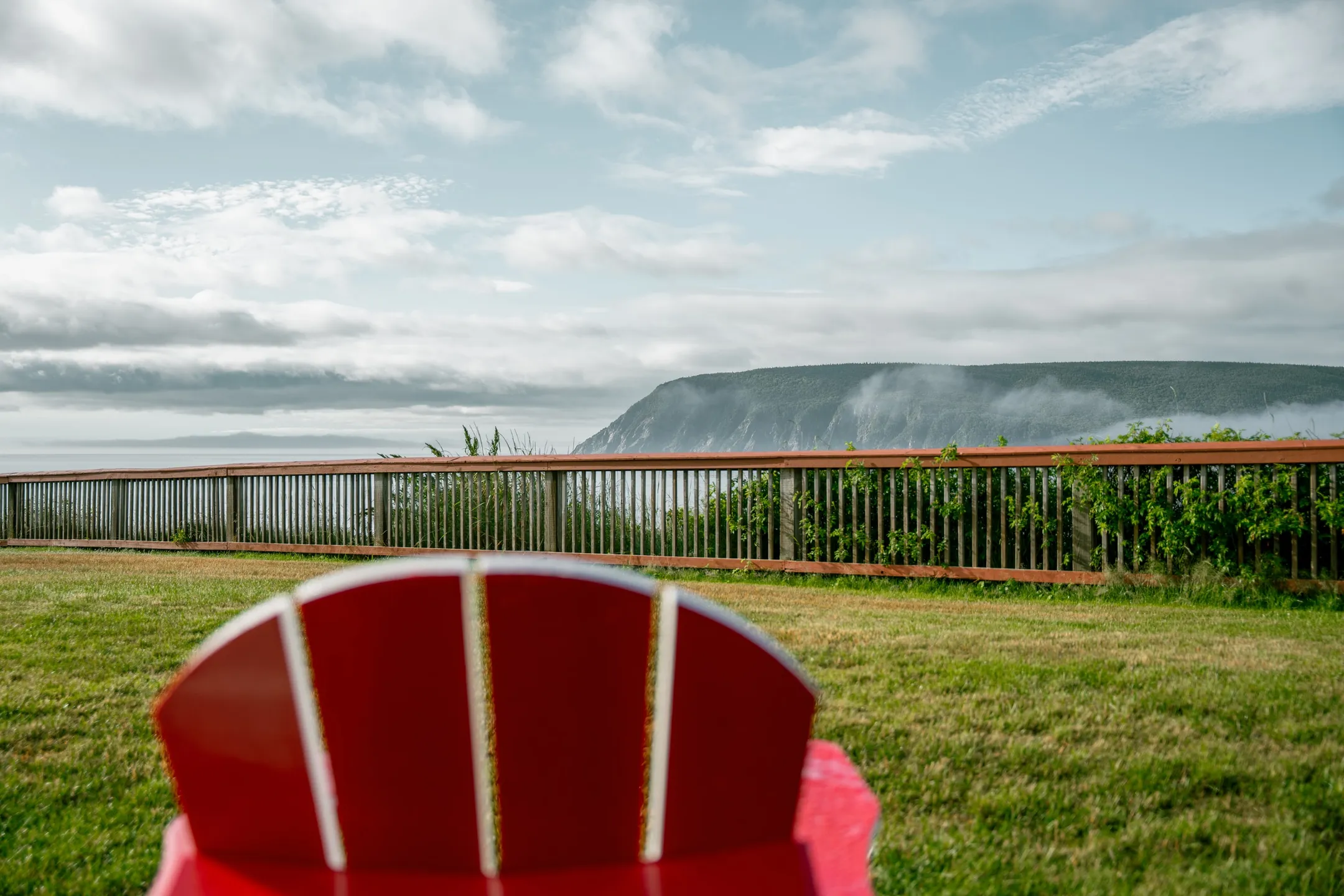 A red chair on the lawn facing a wooden railing, with Cape Smokey across the water.